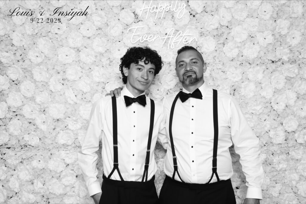 Bride and groom laughing in front of glam wedding photo booth with black and white portraits