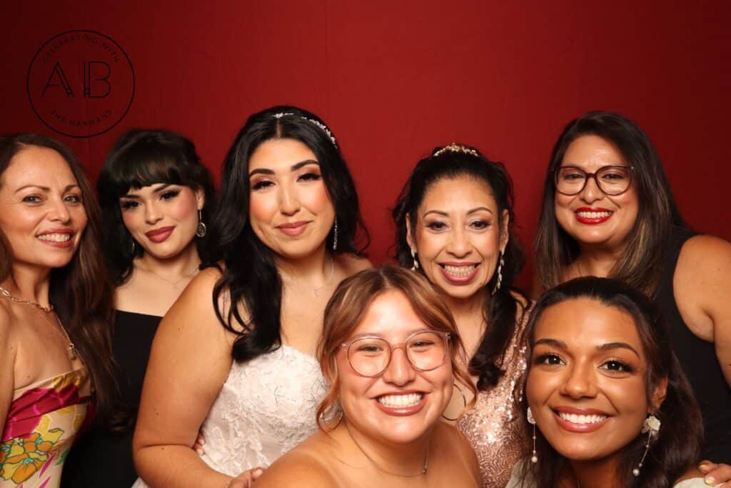 Bride and wedding guests smiling in front of red backdrop during Lake Mary wedding photo booth session